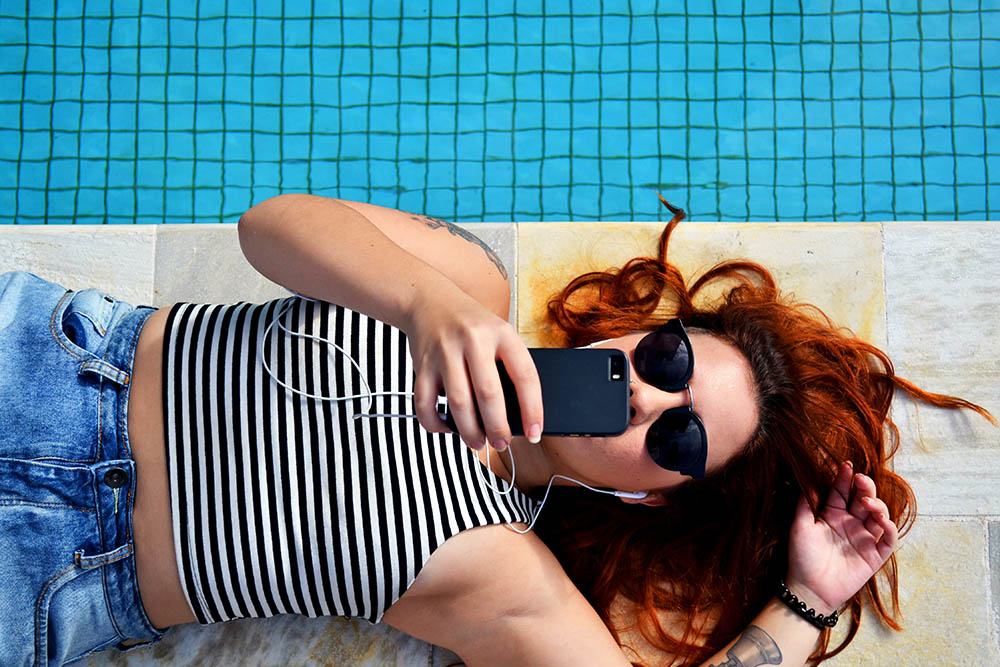 Femme au téléphone avec des écouteurs au bord de la piscine